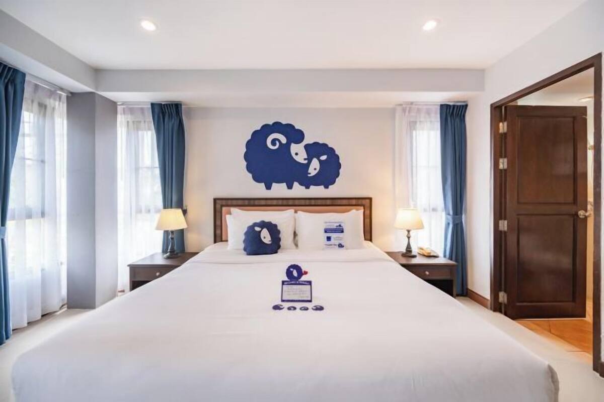 A hotel room with a large bed, two bedside tables with lamps, a wooden door, and a wall decoration of sheep.