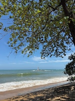 Una playa con un faro, cielo despejado y mar tranquilo.