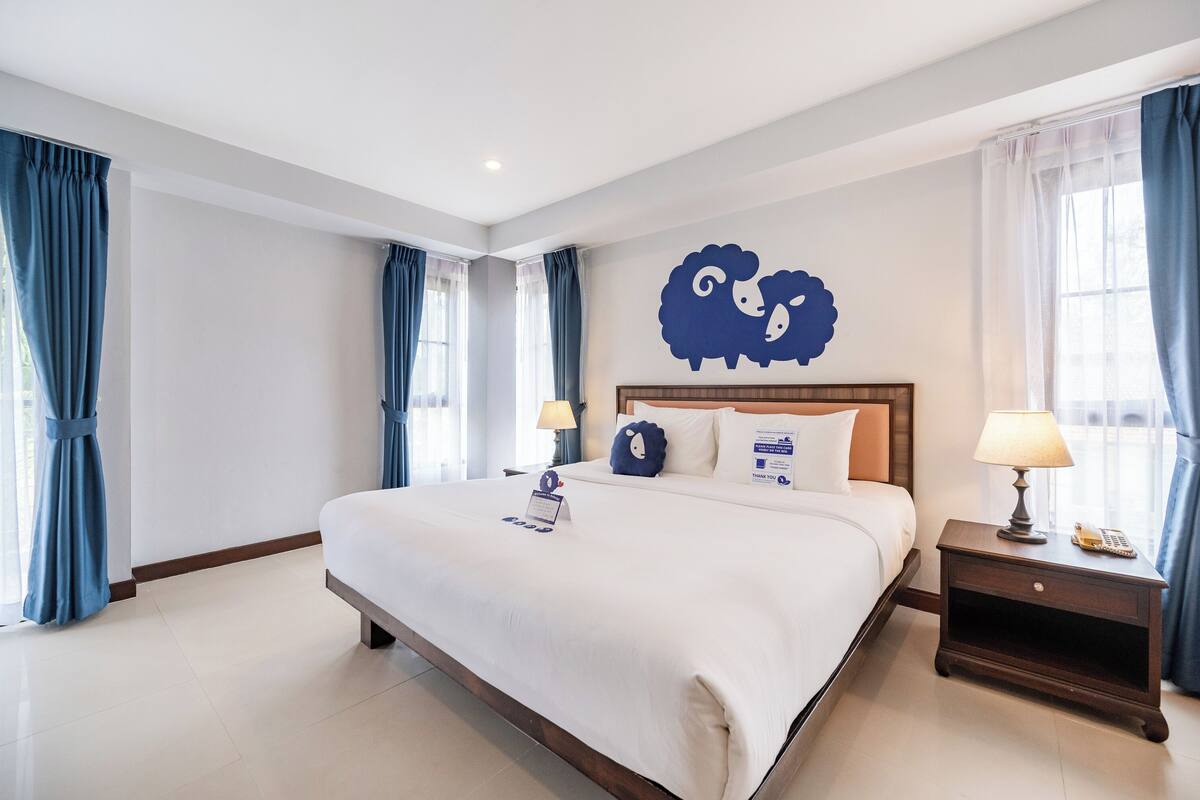 A hotel room with a large bed, a nightstand with a lamp, and a wall decoration of sheep.
