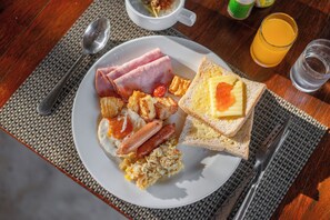Une assiette de petit-déjeuner avec des œufs, du jambon, des toasts et un verre de jus d’orange.