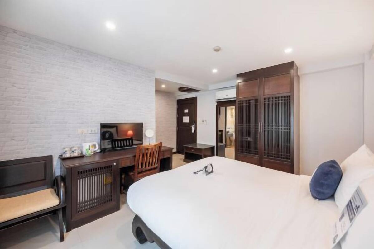 A hotel room with a bed, a desk, a chair, a TV, and a wardrobe.