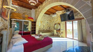 Un dormitorio amplio con una cama grande, una pared de piedra, televisión y balcón.