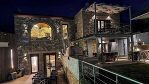 Un edificio de piedra de varios niveles con mesas al aire libre, una barbacoa y un espacio cubierto con vistas al paisaje.