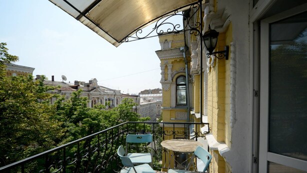 Un balcon avec deux chaises bleu clair et une petite table, d’où l’on peut admirer une vue sur la ville, avec ses bâtiments historiques.