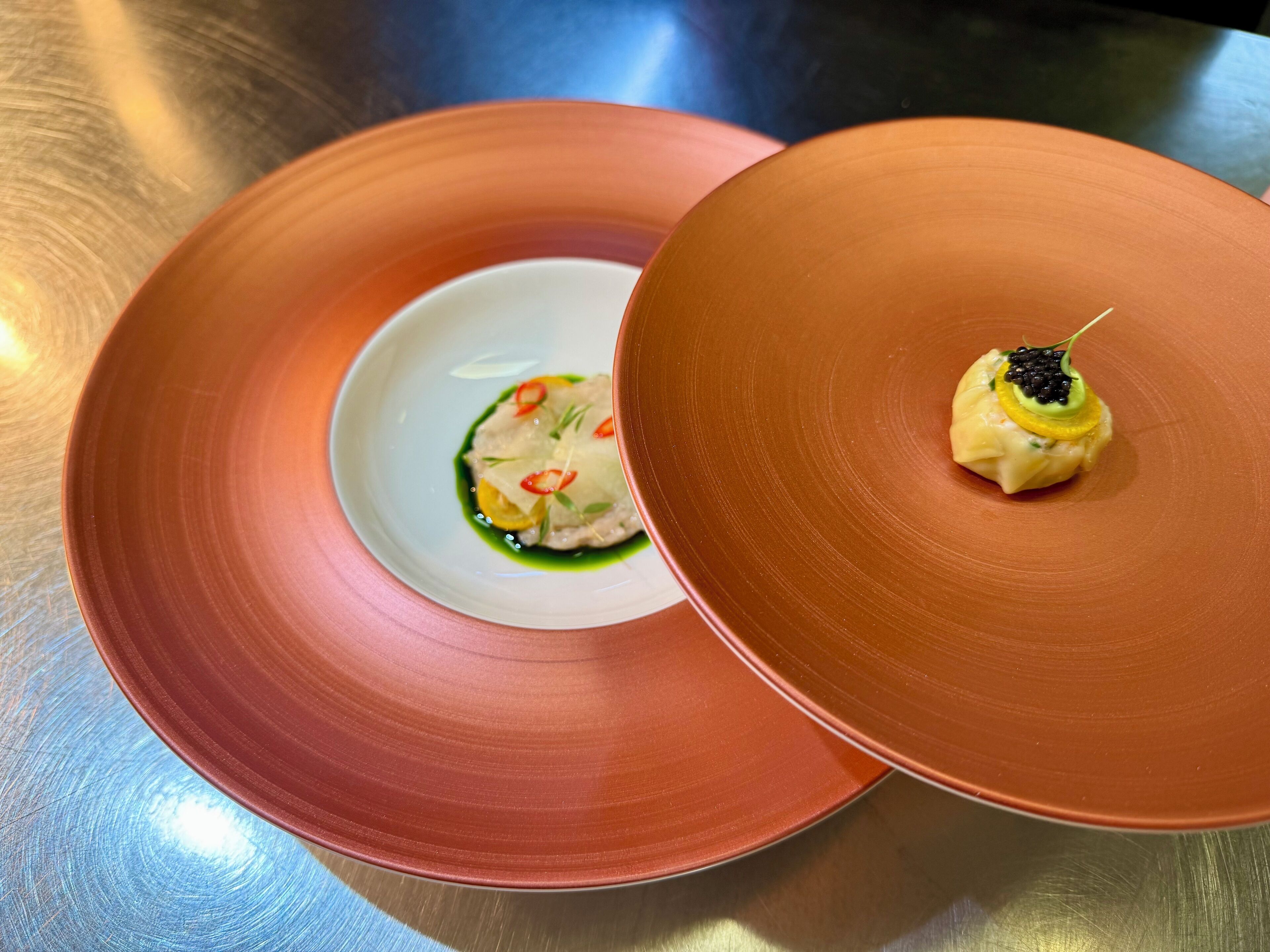 Zwei Keramikteller mit Essen, ein Teller größer als der andere, auf einer Metalloberfläche.