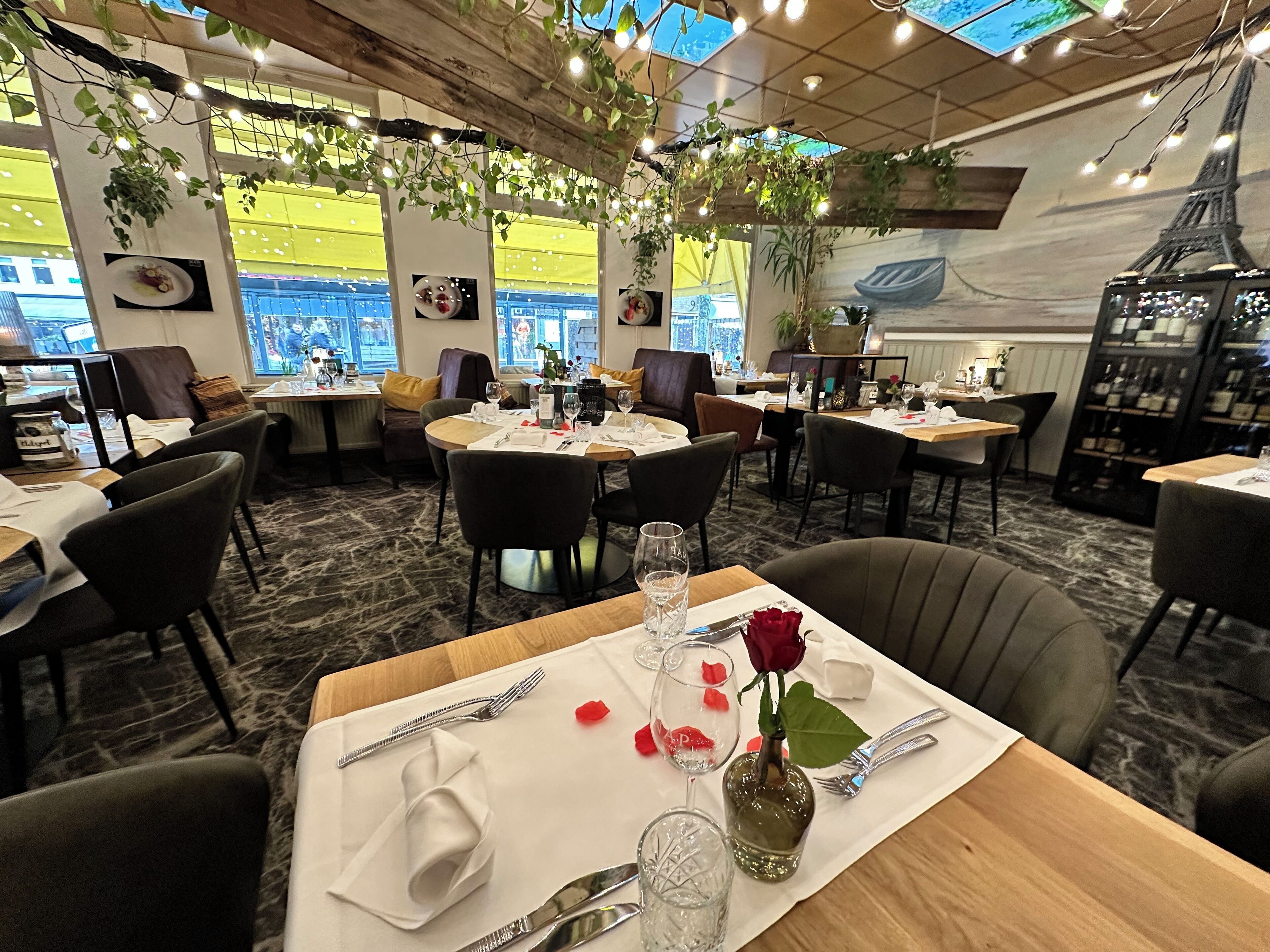 Un restaurante con mesas redondas, sillas y vistas a la Torre Eiffel a través de amplios ventanales.