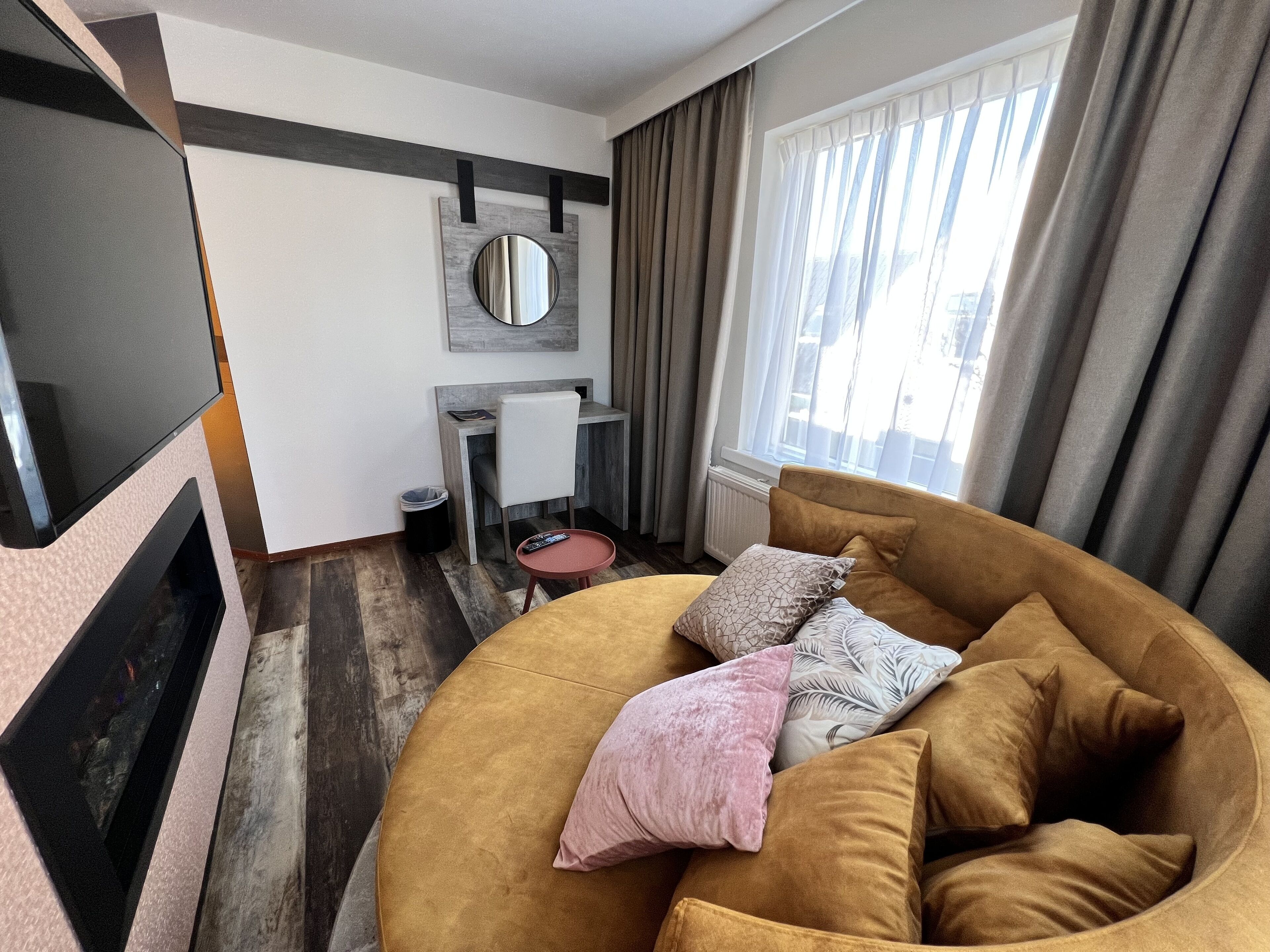 A modern living room with a large round sofa, a TV, a small table, and a desk.
