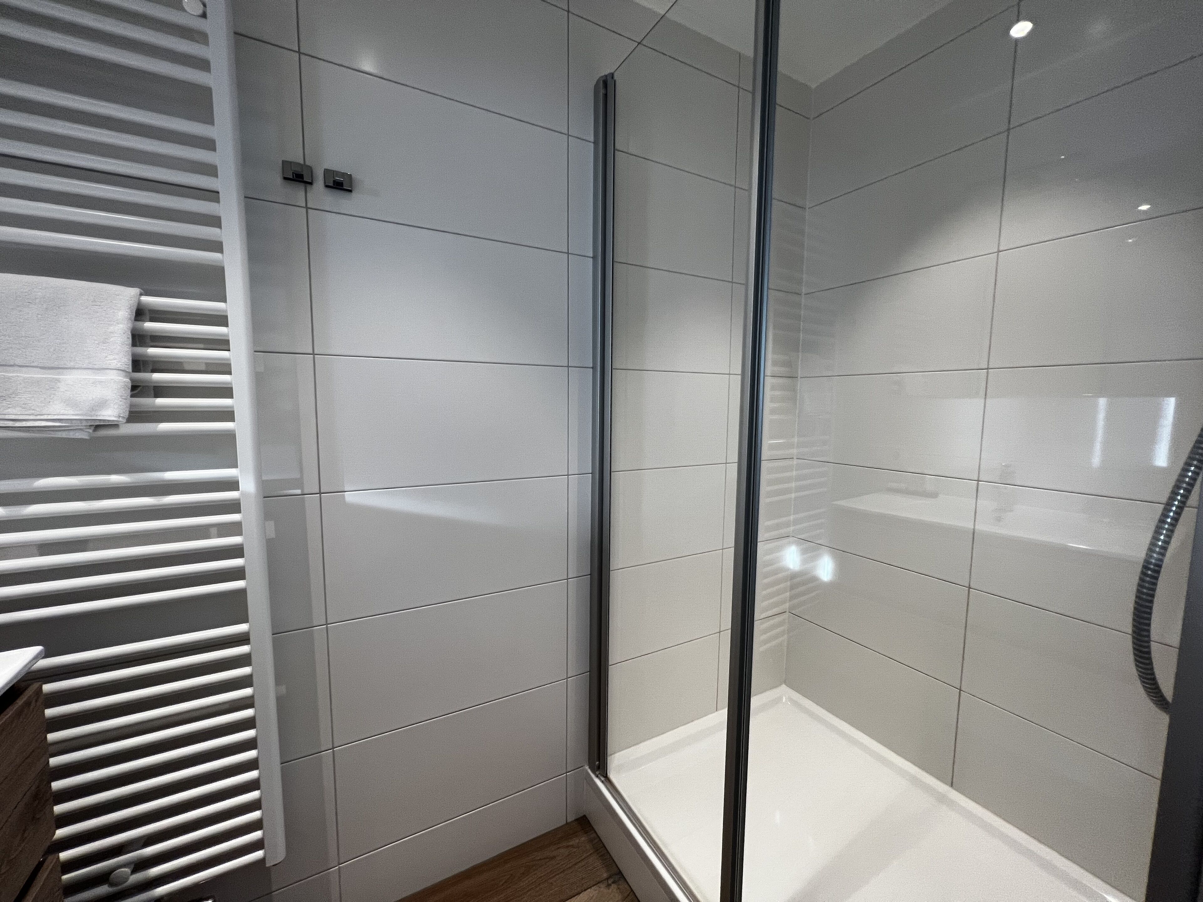 A modern bathroom with a glass shower enclosure, white tiled walls, and a built-in towel rack.