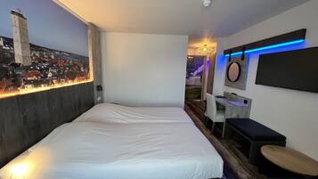 Una habitación de hotel moderna con una cama grande, un escritorio y un mural de paisaje urbano en la pared.