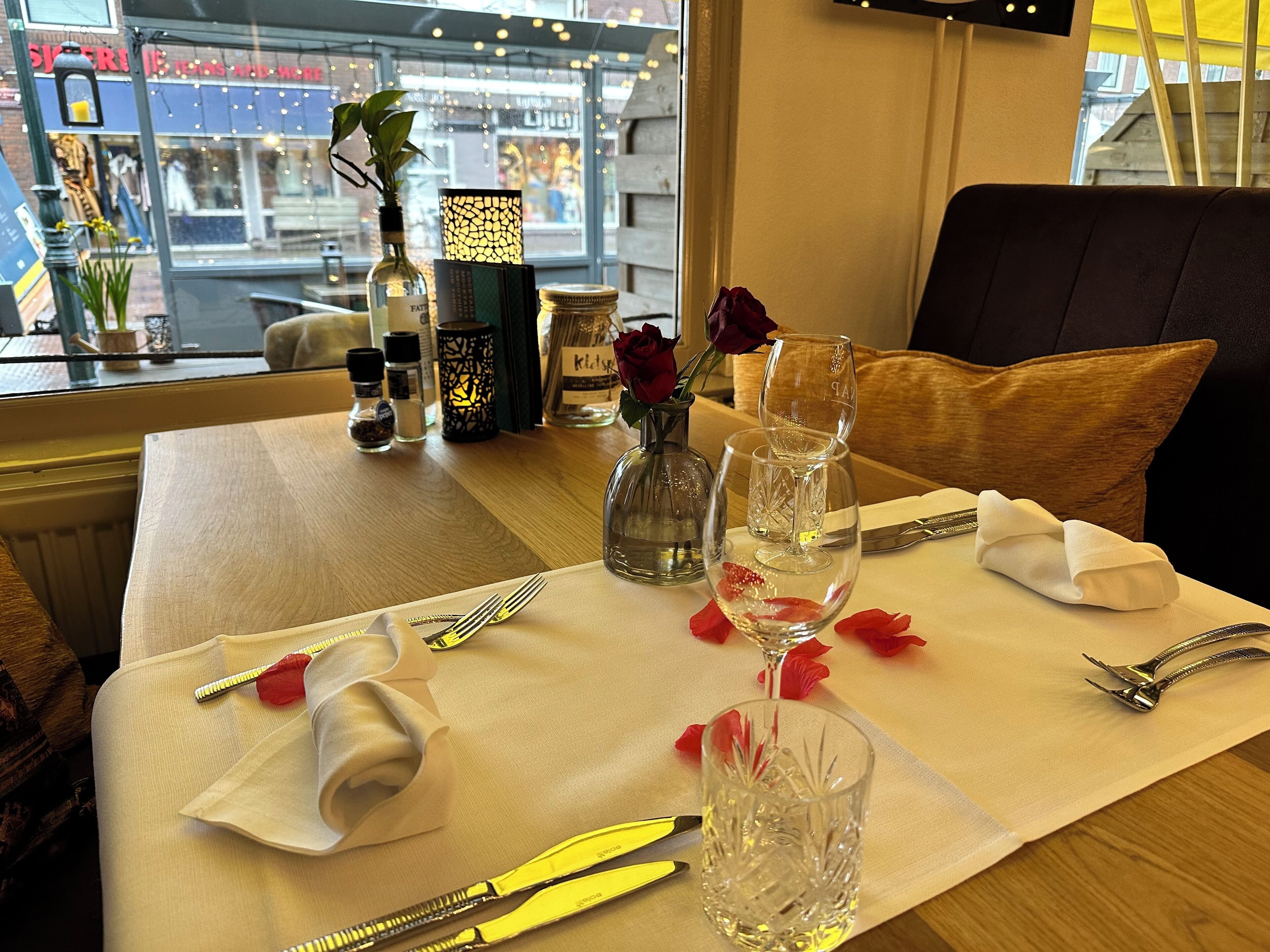 A dining table set with a vase of red roses, wine glasses, and cutlery.