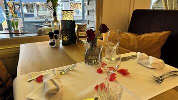 A dining table set with a vase of red roses, wine glasses, and cutlery.
