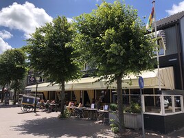 Un café con terraza, un letrero que dice 'cafe/restaurante' y una bandera en un asta.