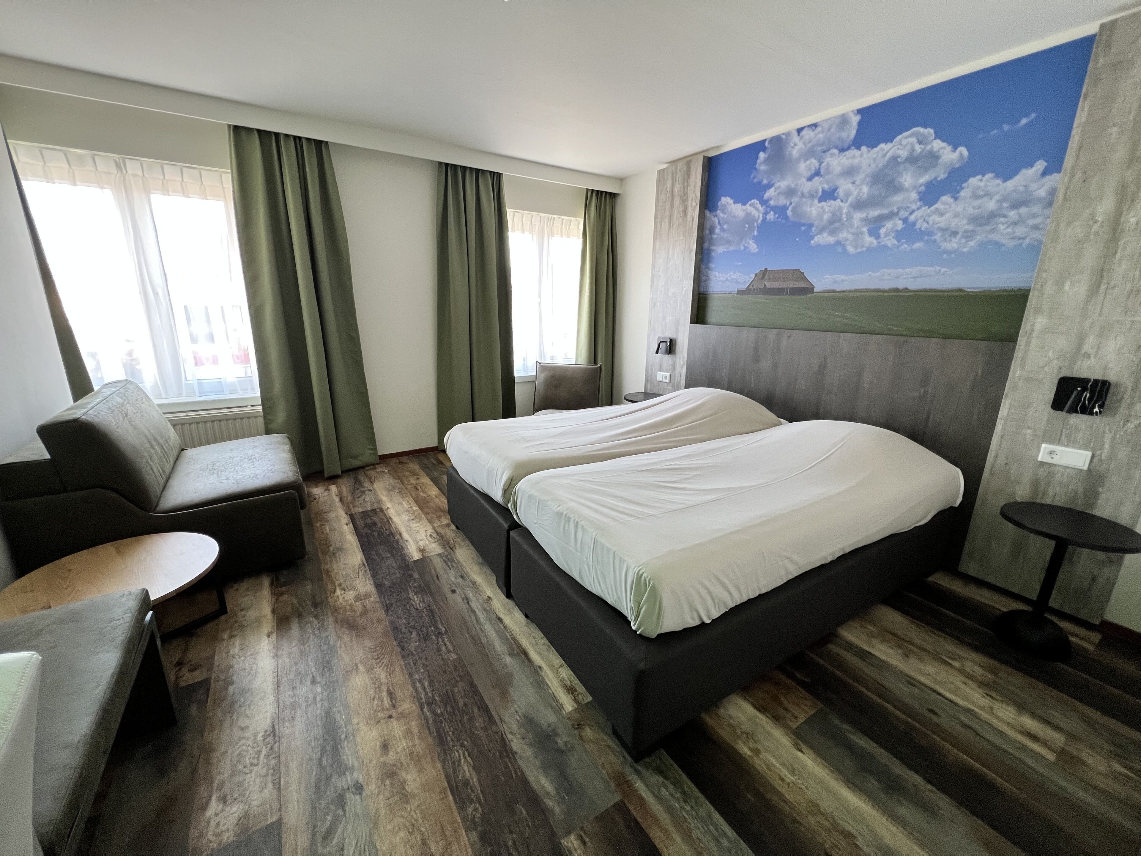 Ein Hotelzimmer mit einem großen Bett, einem Sofa, einem kleinen Tisch und einem Landschaftsbild an der Wand.