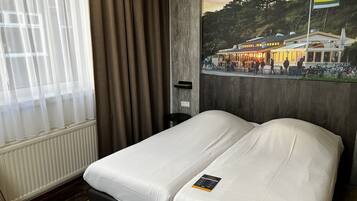 Una camera d'albergo con un letto, una finestra con tende, un termosifone e un murale raffigurante un edificio con persone e biciclette.