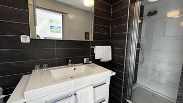 Un bagno moderno con un mobile lavabo bianco, uno specchio grande, una doccia con porta in vetro e pareti rivestite di piastrelle scure.