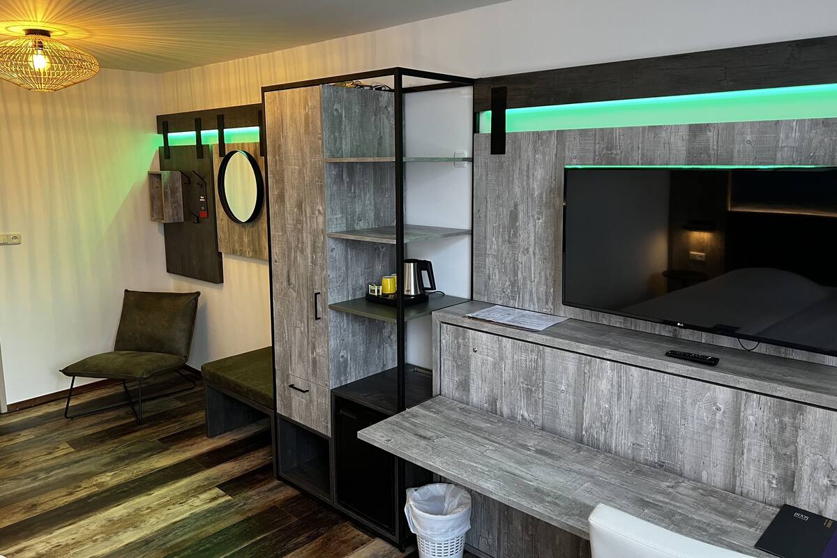 A modern room with a bed, a desk, and a TV. There are shelves and a chair.