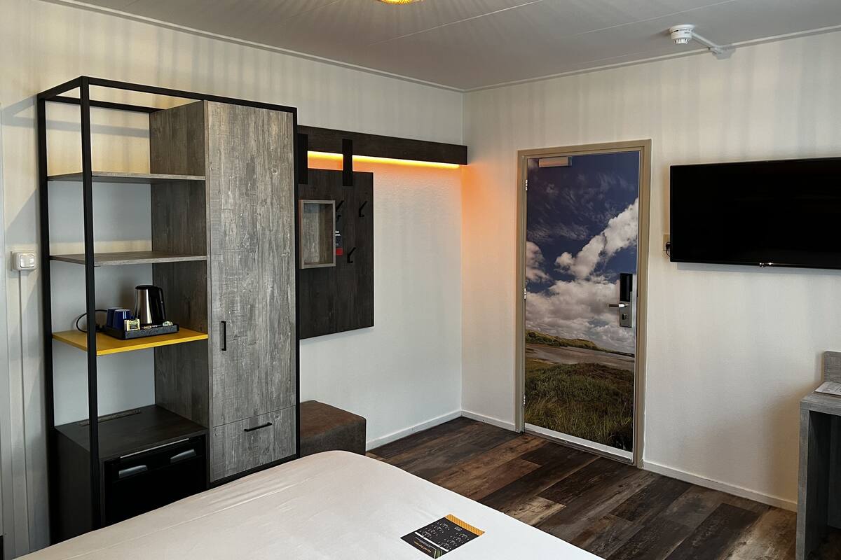 A modern bedroom with a bed, a wardrobe, a television, and a door with a scenic view.