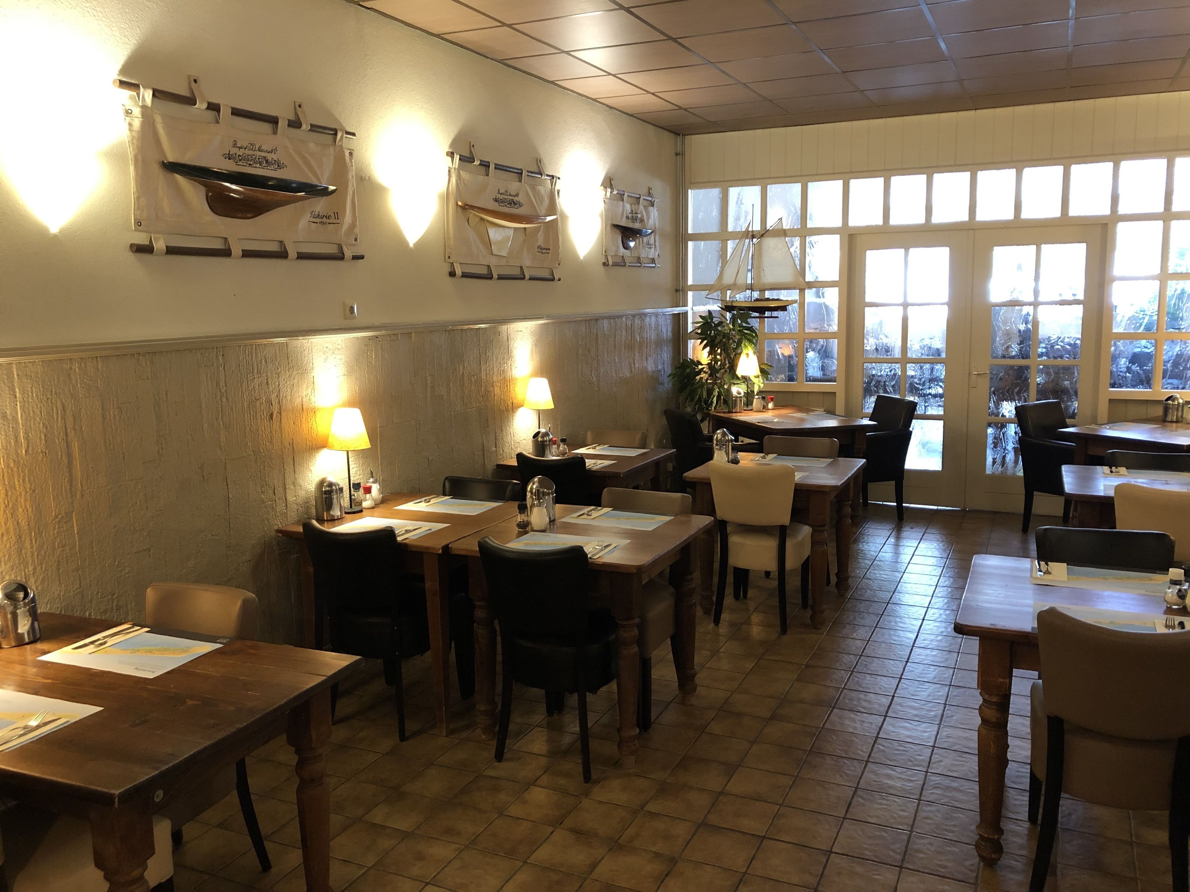 A restaurant with wooden tables and chairs, warm lighting, and large windows.