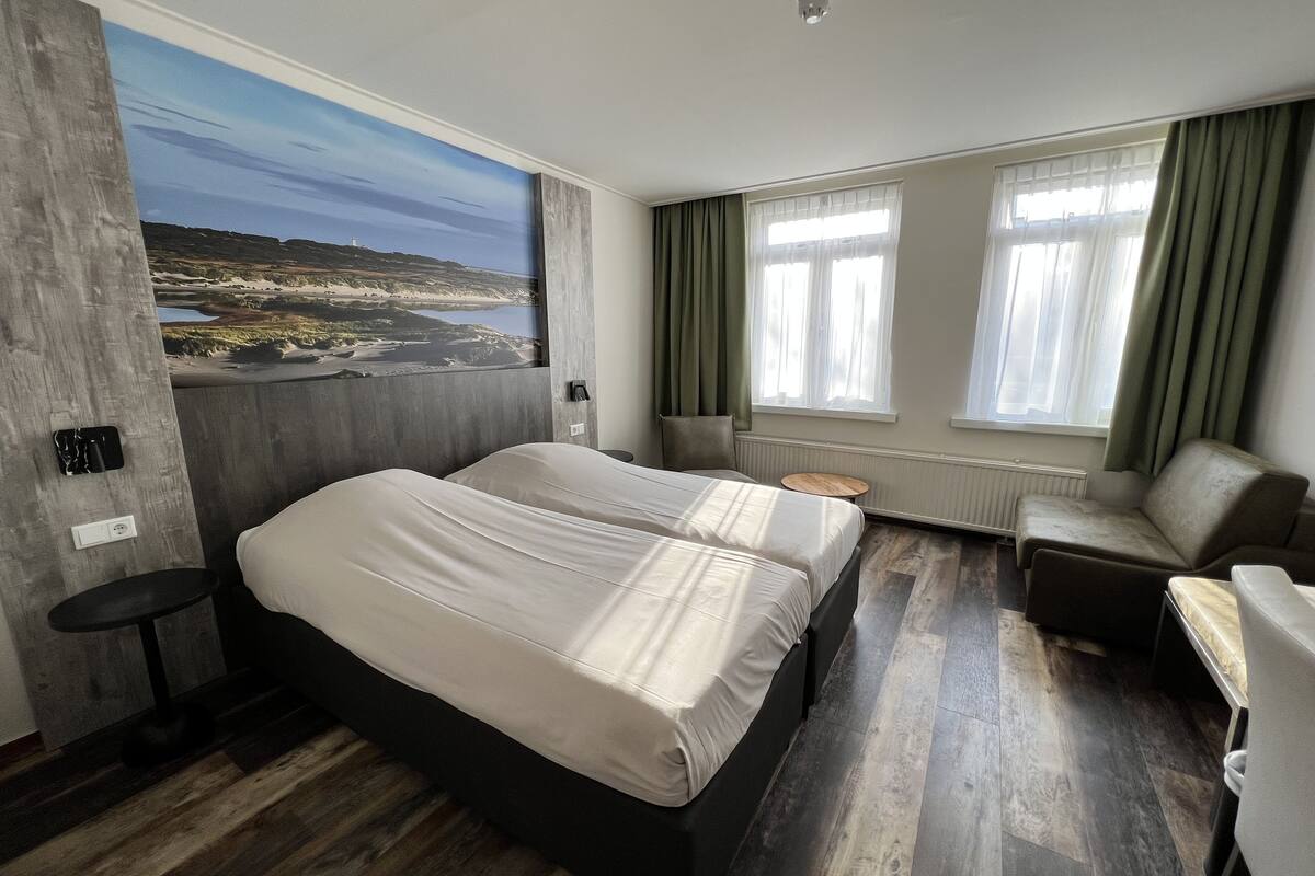 A hotel room with a large bed, a seating area, and a view of a landscape through a window.