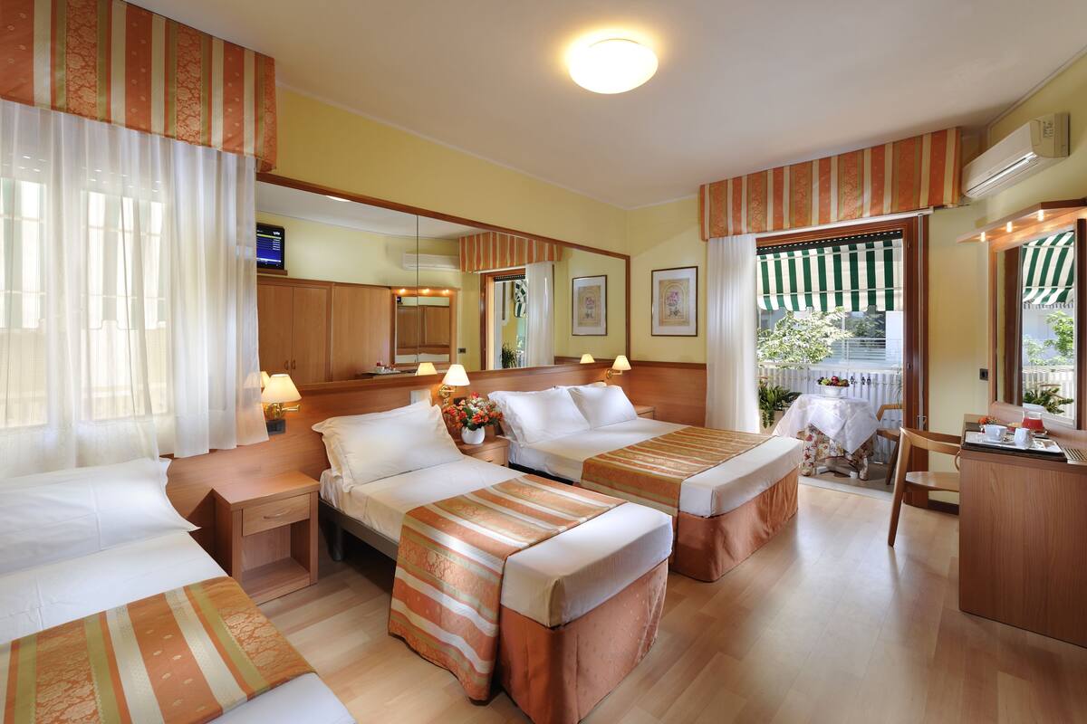 Une chambre d’hôtel avec deux lits, un bureau en bois, une petite table et une grande fenêtre avec des rideaux.