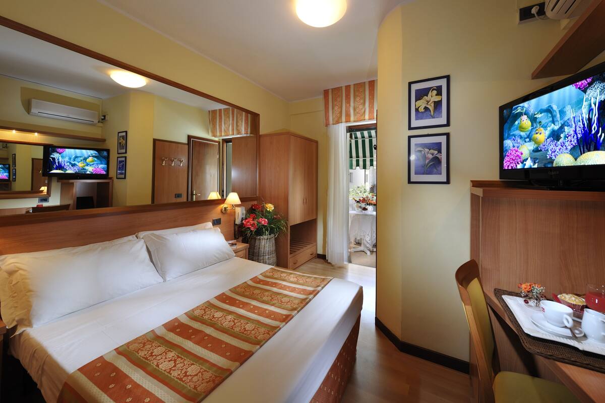 Une chambre d’hôtel avec un grand lit, une télévision, une table à manger avec une chaise, et une salle de bain visible à travers une porte ouverte.