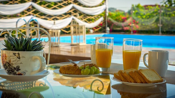 A breakfast setting with a table, a plant, a plate of croissants, a plate of grapes, and two glasses of orange juice. - Villa Natura  Private pool and Sea view -early book 60dates or more 5%  DISCOUNT (Λιθακιά)