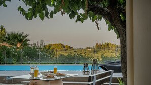 An outdoor dining area with a table set for two, a glass of orange juice, and a bowl of food. - Villa Natura  Private pool and Sea view -early book 60dates or more 5%  DISCOUNT (Λιθακιά)