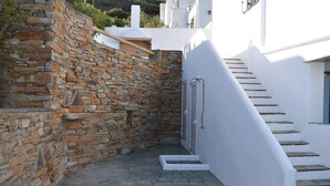 Une cour bordée de murs en pierre, avec un escalier blanc menant à un bâtiment.