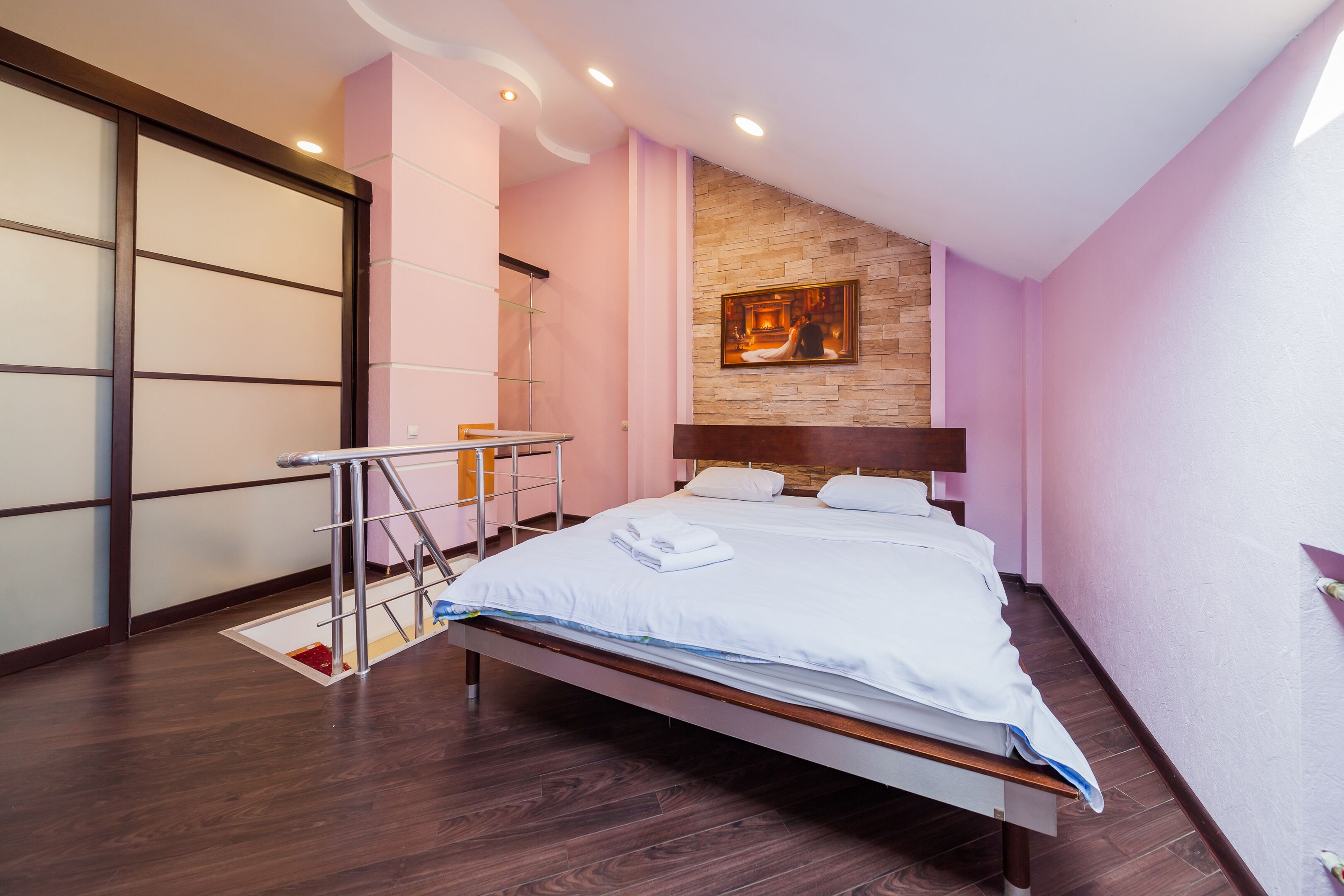 A modern bedroom with a wooden bed, a small table, and a stone accent wall.