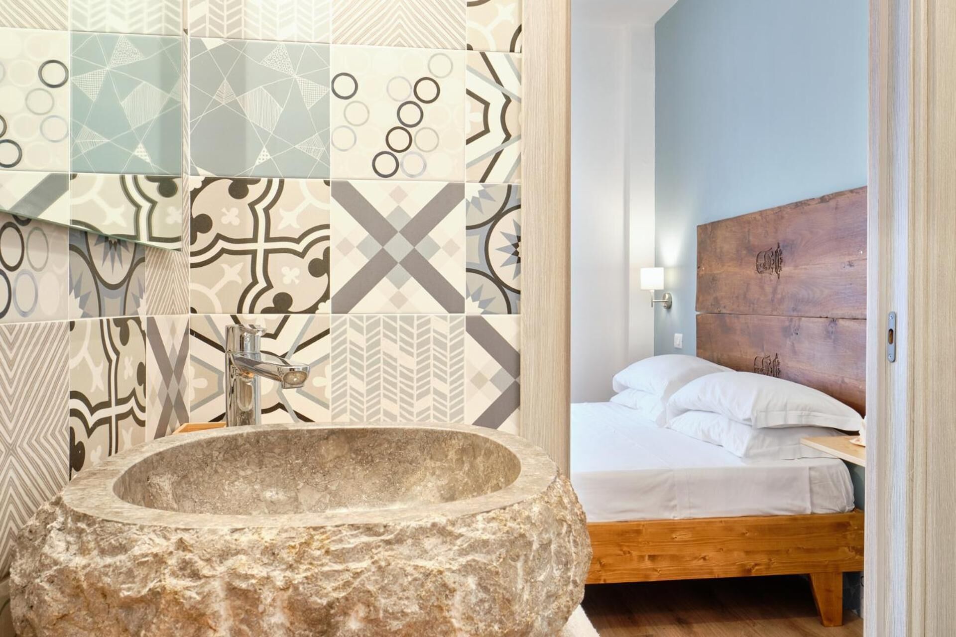 A bathroom with a stone sink, patterned tiles, and a wooden headboard in a bedroom.