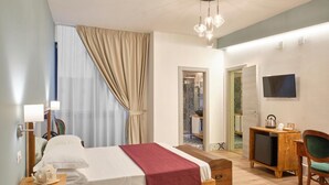 A hotel room with a bed, bedside table, lamp, TV, and a desk with a chair. - La Via Del Porto (Agropoli)