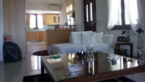 A modern living room with a glass coffee table, a sofa, and a dining area with wooden cabinets. - Welcome To Our Traditional Experience House (Ρέθυμνο)