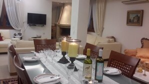 A dining area with a table set for four, candles, wine bottles, and a flat-screen TV mounted on the wall. - Welcome To Our Traditional Experience House (Ρέθυμνο)