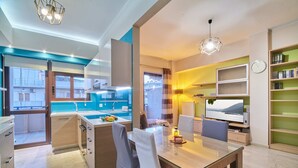 A modern kitchen with a central island, a dining area with a glass table, and a living space with a TV and bookshelves. - Modern Apartment, just 70 meters from the sea! (Ρέθυμνο)