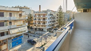 A multi-story building with balconies, a visible chimney, and a street with parked cars and a pedestrian. - Modern Apartment, just 70 meters from the sea! (Ρέθυμνο)