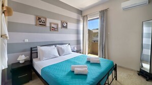 A neatly made bed with a teal bedspread and two towels, a bedside lamp, and a nightstand with a drawer. - Modern Apartment, just 70 meters from the sea! (Ρέθυμνο)