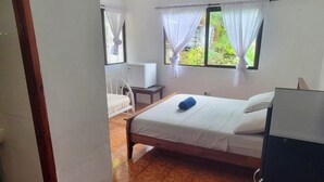 Une chambre à coucher avec un lit, un bureau et une chaise. Il y a une fenêtre avec des rideaux.