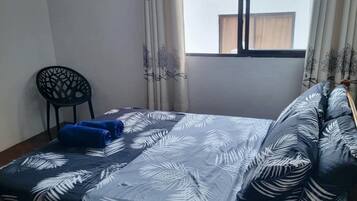A room with a bed, a chair, and a window with curtains.