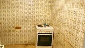 Una cucina piccola e stretta con piano cottura e forno bianchi, pareti piastrellate con motivo floreale e pavimento in legno ricoperto da un tappeto.