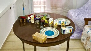 Un tavolo da pranzo con diversi cibi e una ventola in una stanza con finestra e tende.