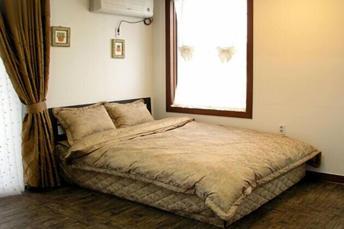 Een eenpersoonsbed met een gewatteerde spreidek, een raam met houten kader en een luchtverwarmer aan de muur.