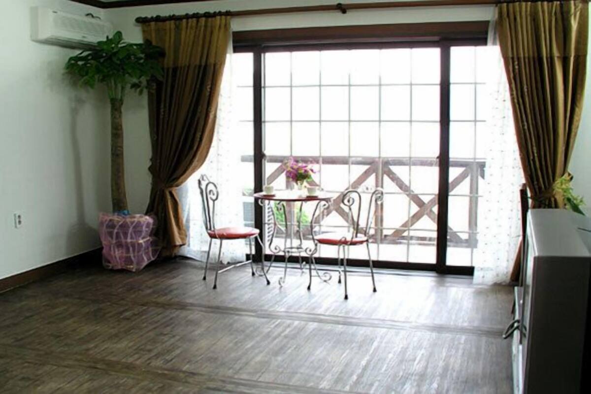 Een balkon met een tafel en stoelen, een plant in pot en uitzicht op een gebouw door een raam.