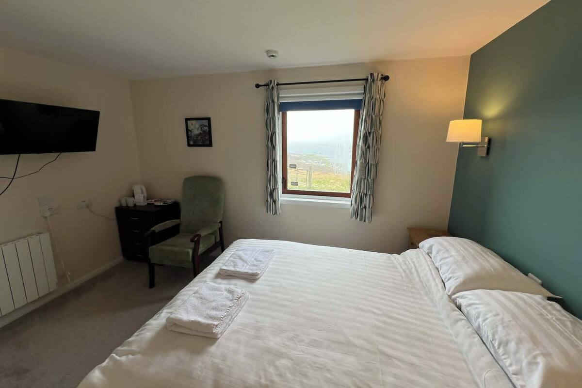 A hotel room with a bed, a chair, a desk, a TV, and a window with curtains.
