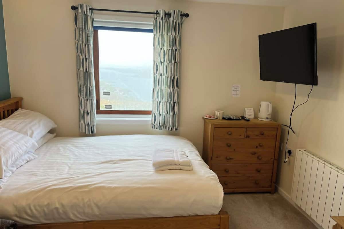 A bedroom with a bed, a dresser, a television, and a window with curtains.
