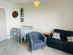 Een woonkamer met een eettafel, stoelen, een bank en een wandplank met decoratieve objecten.