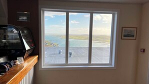 A room with a large window offering a view of a coastal landscape, a wooden counter, and a ceiling with recessed lighting. - The Westings (Whiteness)