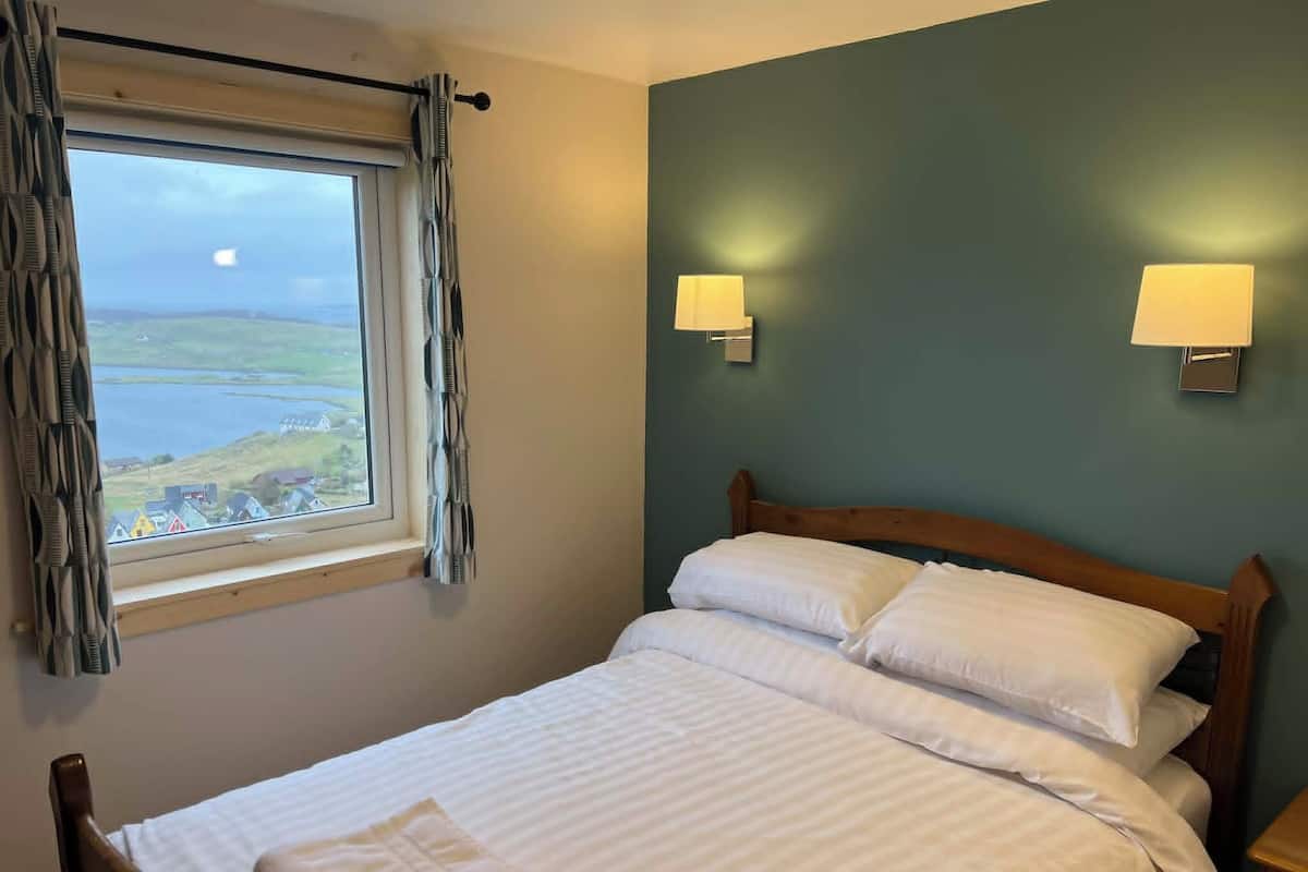 A bedroom with a bed, a window with curtains, and two wall-mounted lamps.