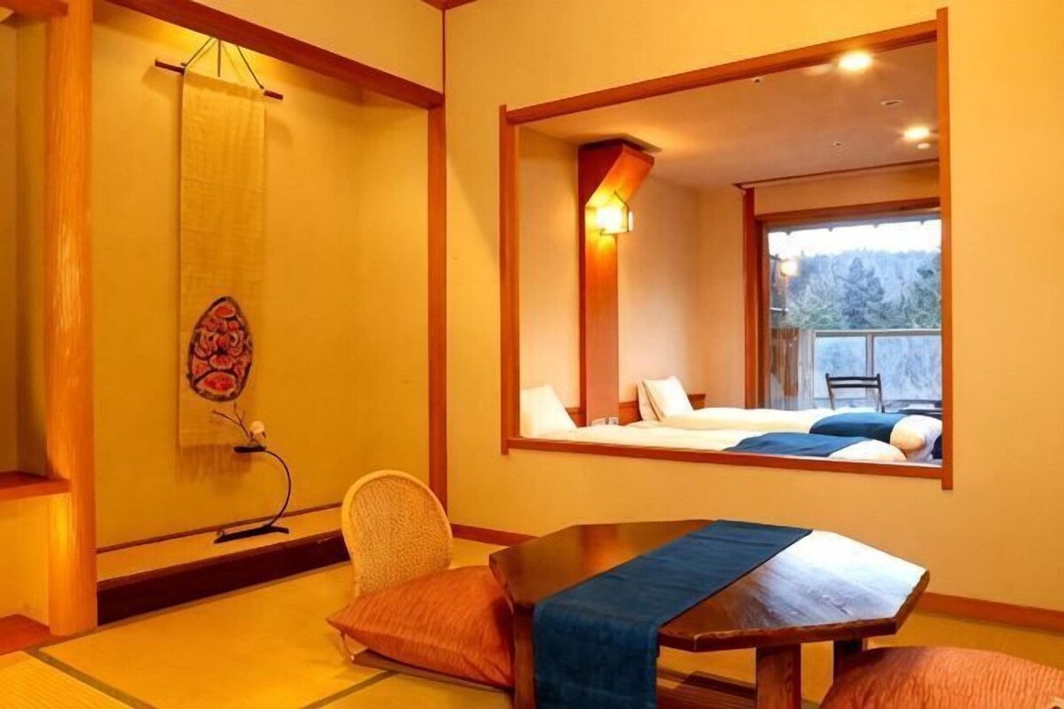 A traditional Japanese-style room with tatami flooring, a low table, and a bed with a view of the outdoors.