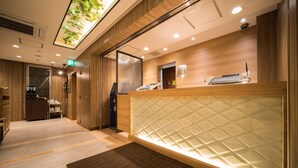 A reception area with a wooden reception desk, a glass partition, and a ceiling with a green plant installation. - Super Hotel Hachinohe Nagayokocho (Hachinohe)