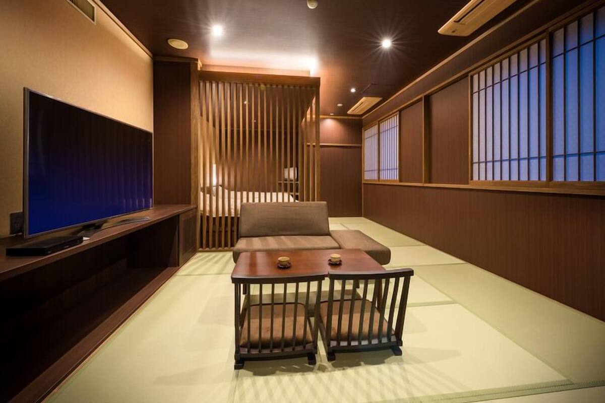 A traditional Japanese-style room with tatami flooring, a low table with cushions, a television, and sliding doors.